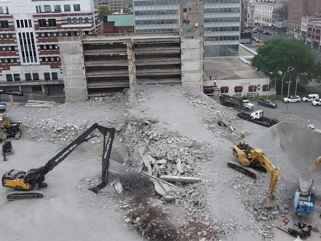 Aerial view of the parking garage teardown with two excavators on the rubble and the glass office tower behind