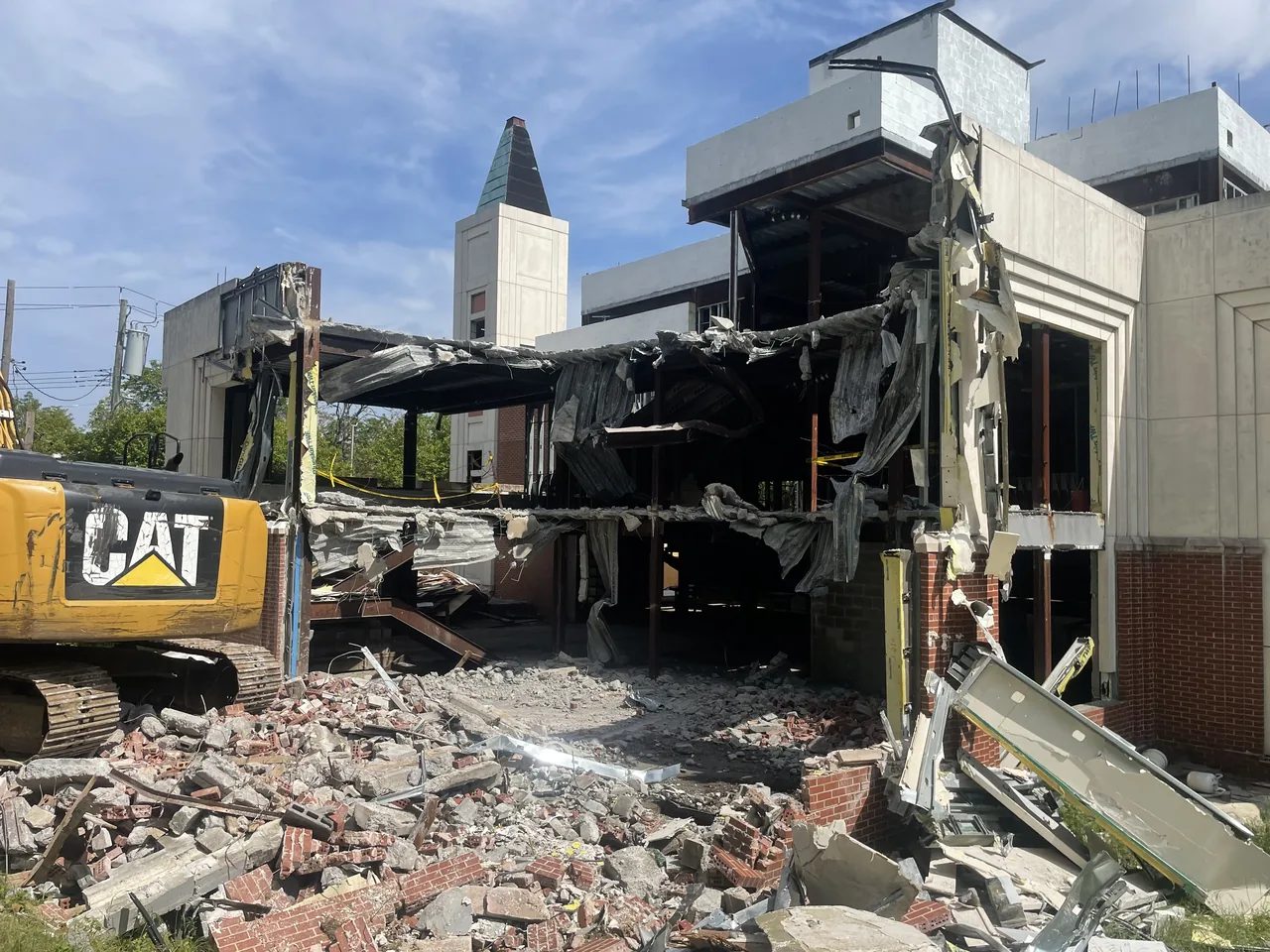 Excavator beside a two story commercial building torn open to its steel frame, brick and block rubble in front, commercial demolition