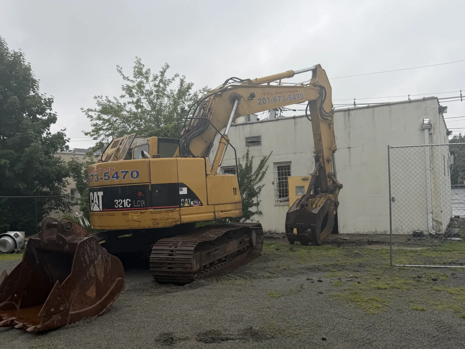 Excavator with a grapple at the wall of a block building on a bare lot