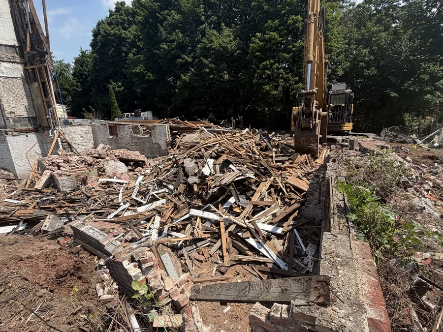 Excavator behind a pile of wood framing and brick inside the old foundation walls of a torn down house, debris removal