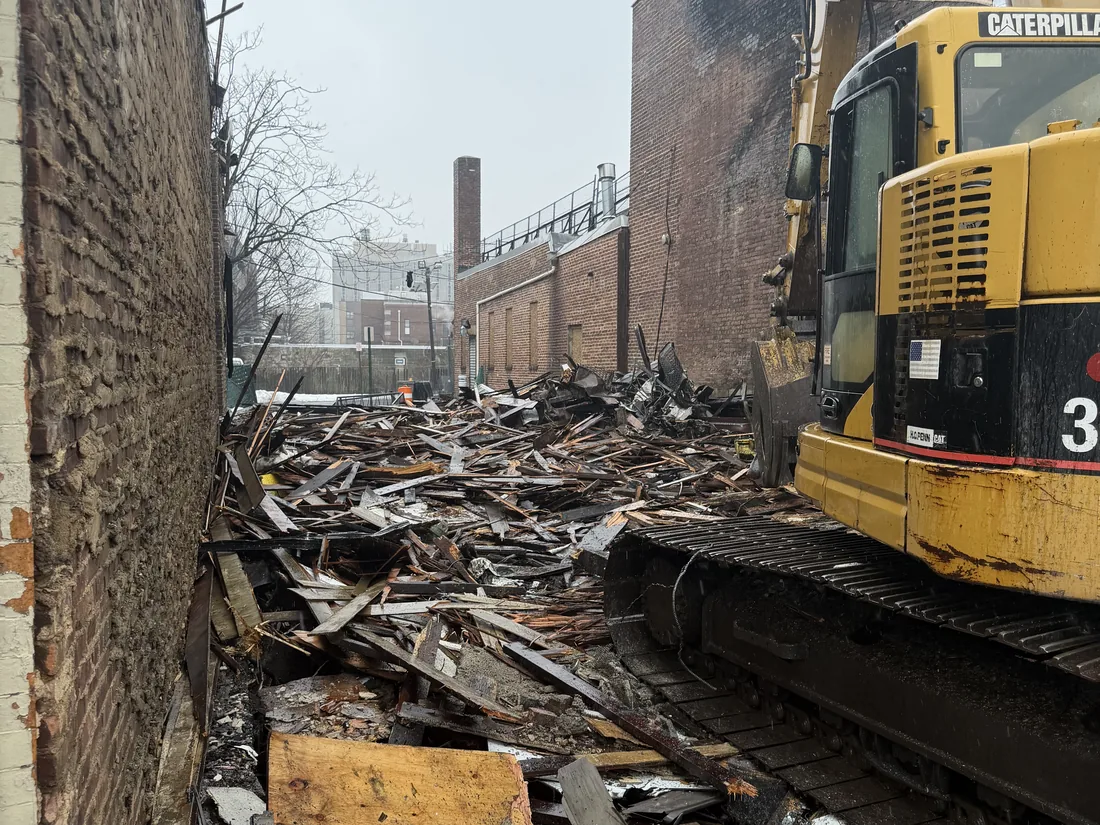 Excavator loading charred fire debris between the brick walls of the buildings on either side