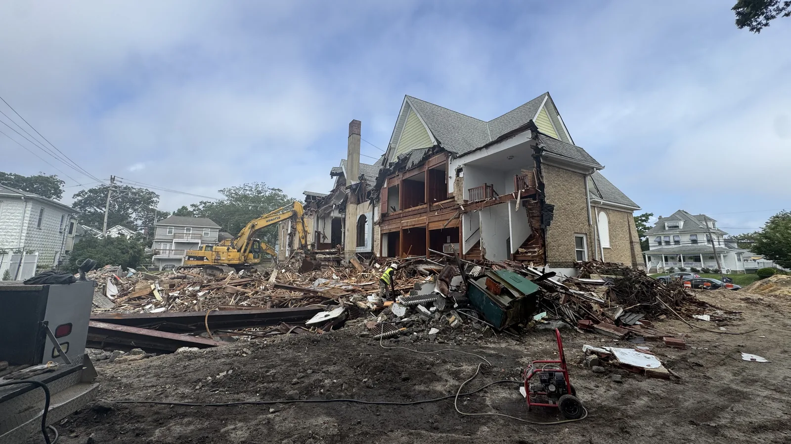 Excavator taking down a church with its side torn open, a crew member in the debris and a pressure washer in front, demolition contractor
