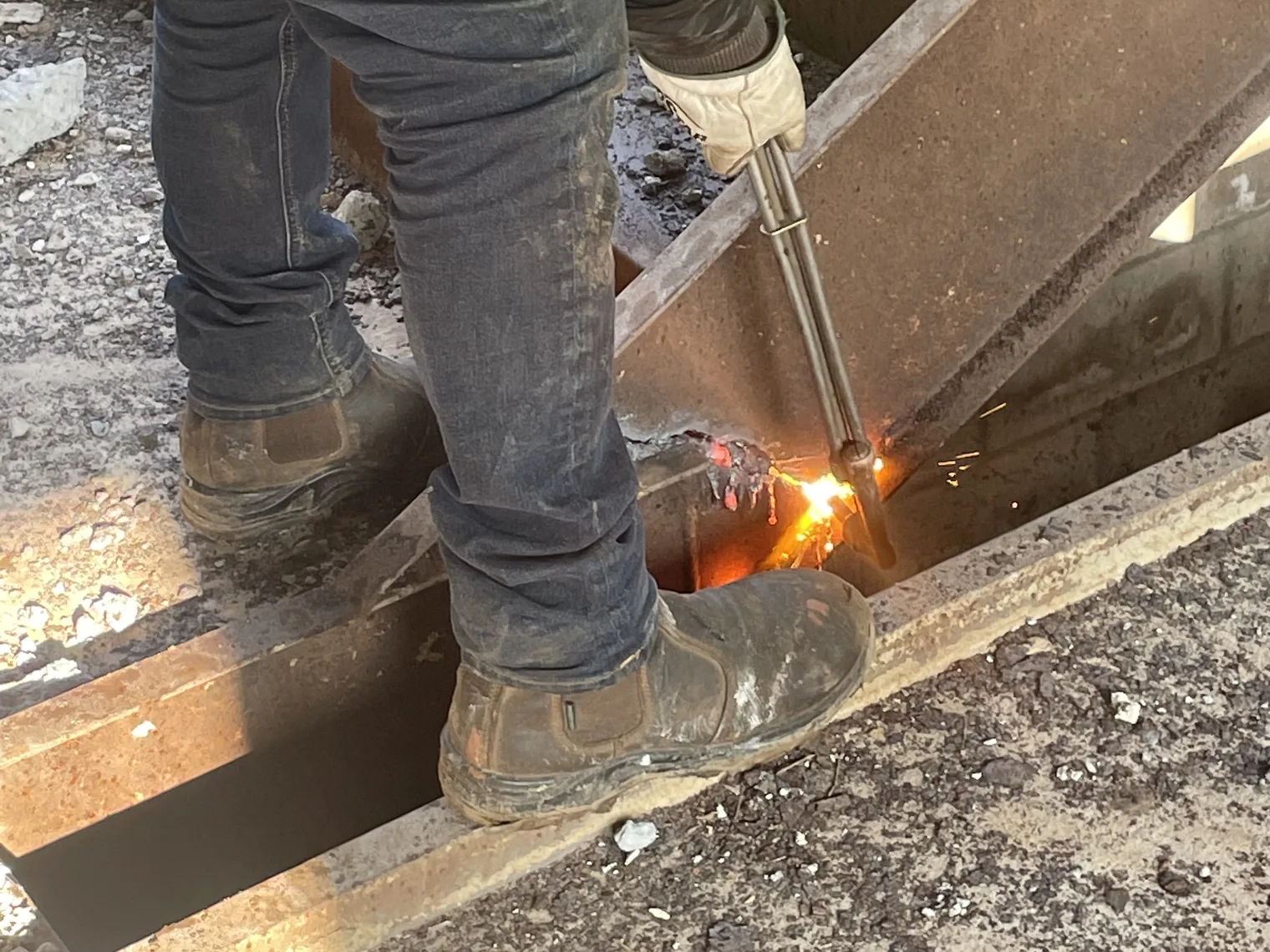 Worker in a high visibility vest cutting a steel beam with a torch, sparks flying, industrial demolition