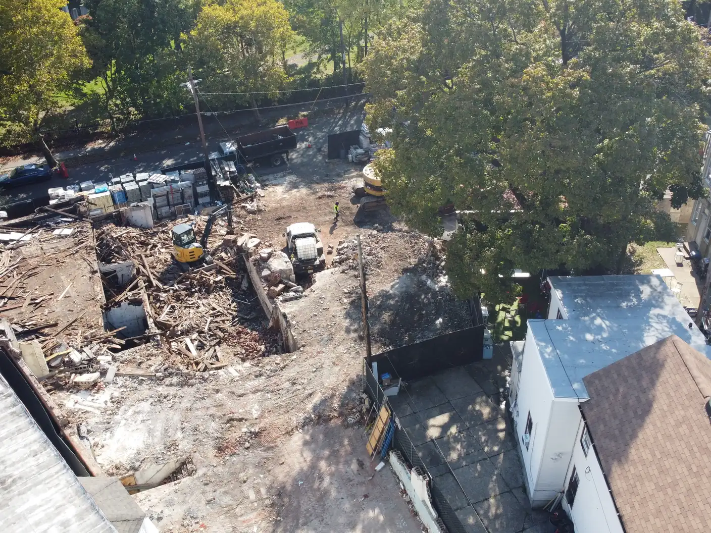 Aerial view of two excavators working a pile of wood framing and brick on a fenced teardown lot