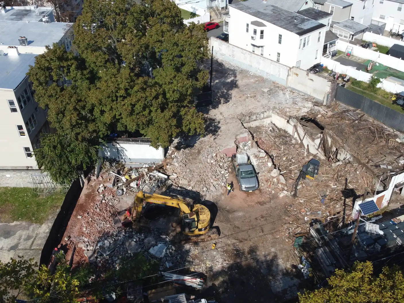 Aerial view of a teardown lot cleared to the old foundation walls, an excavator and a pickup inside the fence