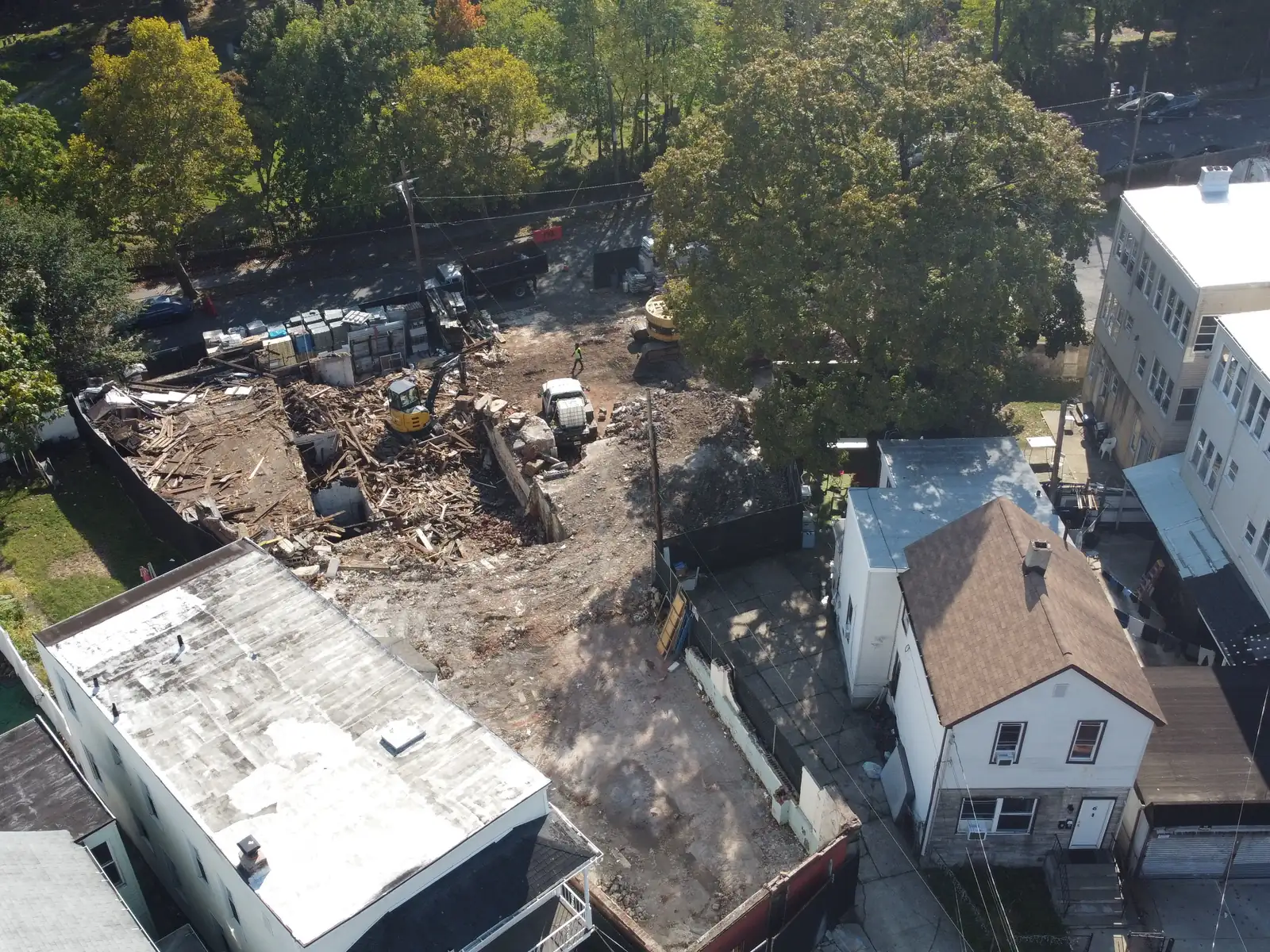 Aerial view of a building taken down between a three story building and a house, a mini excavator on the wood debris
