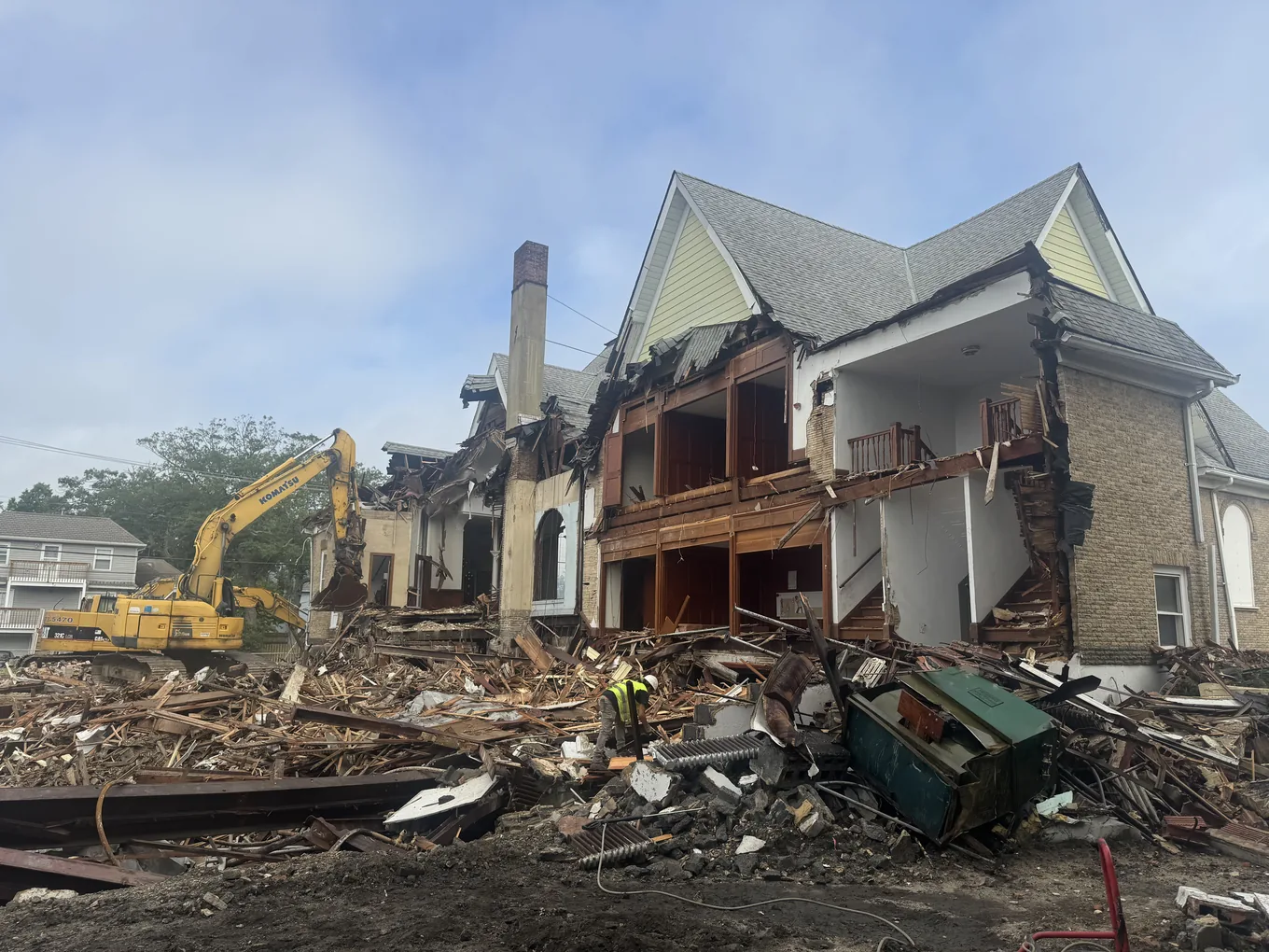 Church with its side wall torn open, the excavator at the pile of brick and timber in front