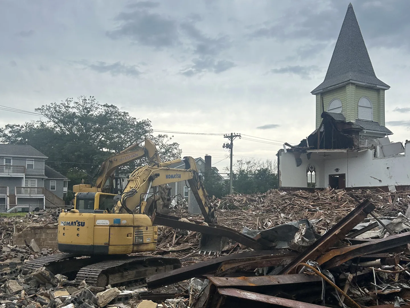 Excavator at a pile of steel beams and debris under the church steeple on an overcast day
