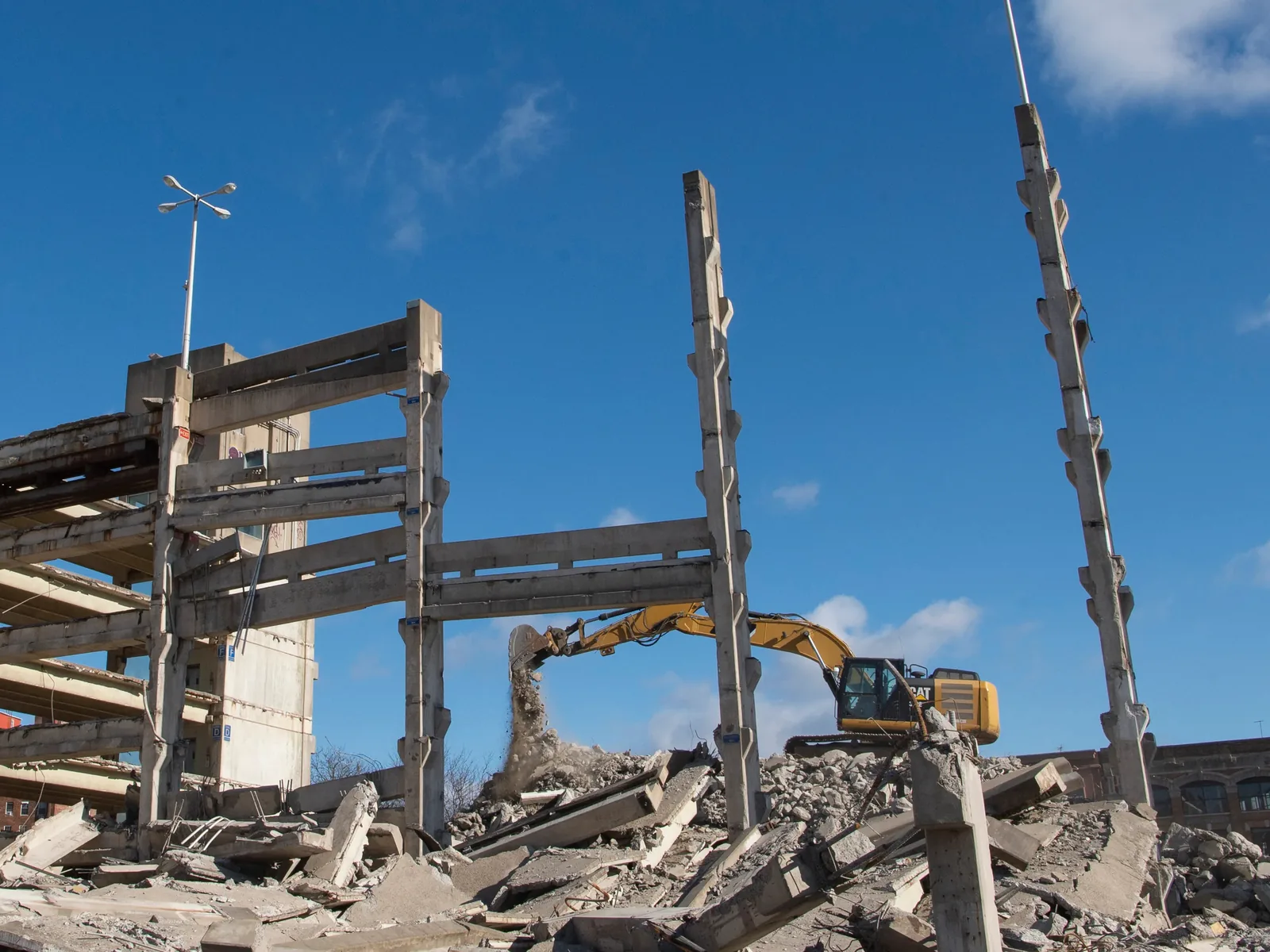 Excavator dropping rubble beside the last standing columns of the parking garage